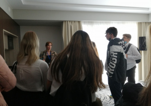 Grupa uczniów słucha informacji pracownika hotelu, w jednym ze zwiedzanych pokoi